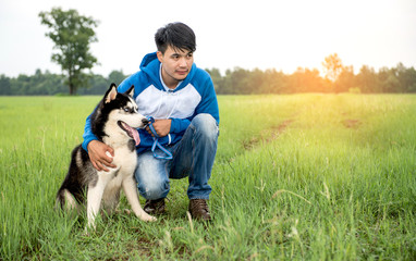 Naklejka na ściany i meble Man and dog Siberian huskies concept. Asian young man with his dog on meadow.