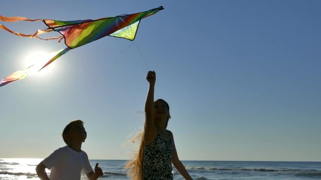Happy children with mom fly a kite on the beach. The family plays and rests together in nature. Hold by hand. Beautiful day and blue sky by the ocean.
