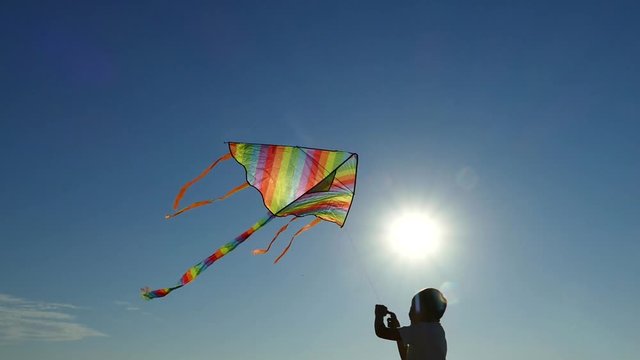 Happy children with mom fly a kite on the beach. The family plays and rests together in nature. Hold by hand. Beautiful day and blue sky by the ocean.