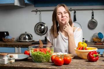 Obraz na płótnie Canvas young girl prepares a vegetarian salad in the kitchen, she licks her finger and tastes, the process of preparing healthy food