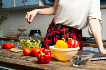 young girl prepares a vegetarian salad in the kitchen, she adds sliced ingredients to the plate,...