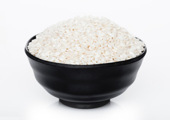 Black bowl of raw organic arborio risotto rice on white background. Healthy food.