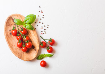 Organic Cherry Sugardrop Tomatoes on the Vine with basil and pepper in oilve wood plate on white...