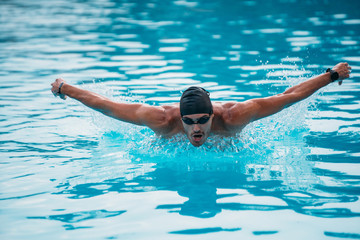 Professional man swimming in butterfly style with hat and goggles at the pool