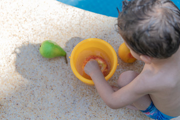 Photo from above of a child putting an apple in a bucket of water.