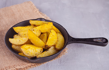 Homemade baked potato wedges with herbs on black iron pan on the gray background. Top view.
