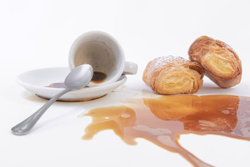 Two freshly baked puff pastry rolls and a cup of coffee spilled over the table