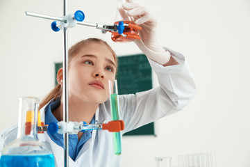 Smart pupil looking at flask with reagent on holder in chemistry class