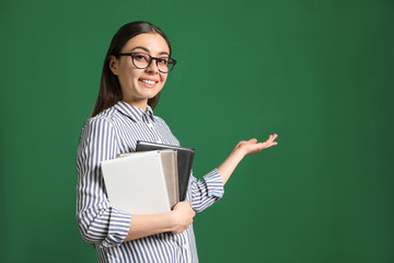Portrait of young teacher with notebooks on green background. Space for text