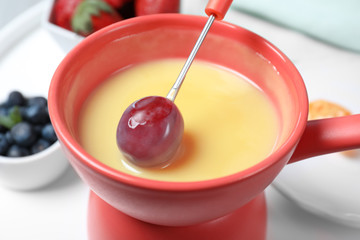 Dipping grape into pot with white chocolate fondue on table, closeup