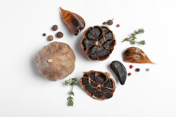 Aged black garlic with thyme and peppercorns on white background, view from above