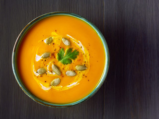 Pumpkin cream soup in a bowl with pumpkin seeds, parsley and cream on wooden table. Traditional autumn, Thanksgiving meal. Healthy organic vegetarian food. Top view, copy space