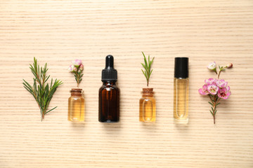 Flat lay composition with bottles of natural tea tree oil on wooden background