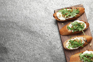 Board with tasty bruschettas on grey table, top view. Space for text