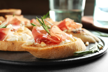 Tasty bruschettas with prosciutto and cream cheese served on table, closeup