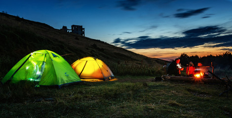 Summer evening in a hike. Glowing tents. Camping in a beautiful location. Sitting around the...