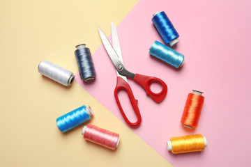 Bobbins of threads and sewing scissors on color background, flat lay