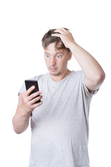 Young casual man in t-shirt clutching his head and looks into the phone in big surprise, isolated on white background.