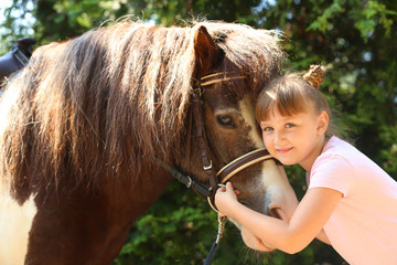 Cute little girl with her pony in green park