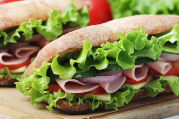 Two sandwiches with fresh vegetables, ham and cheese in ciabatta bread