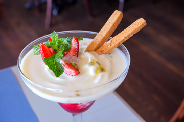 Summer dessert, classic cheesecake with strawberries decorated with mint leaves. On a light blue wooden table, bright sunlight. red fresh strawberries and cream or creamy yoghurt garnished for a tasty