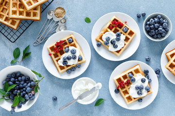 Traditional belgian waffles with cream cheese and fresh blueberry on blue background, top view