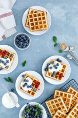 Traditional belgian waffles with cream cheese and fresh blueberry on blue background, top view