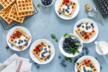 Traditional belgian waffles with cream cheese and fresh blueberry on blue background, top view