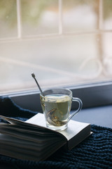 Cozy winter autumn still life: cup of hot tea, warm plaid and opened book on windowsill. Minimal unplug calmness relax concept, seasonal weekend or depression loneliness