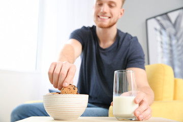 Fototapeta na wymiar Handsome young man eating tasty cookies with milk at home