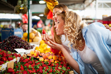 Obraz premium Young women friends baying vegetables and fruits on the market