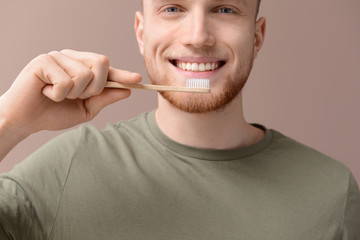 Young man cleaning teeth on color background, closeup