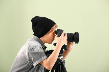 Cute little photographer with professional camera on color background