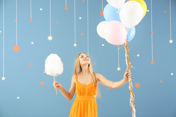 Beautiful woman with cotton candy and air balloons on color background