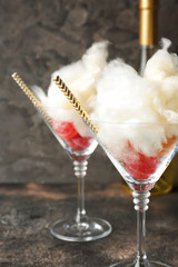 Tasty cotton candy with sweets in glasses on grey background