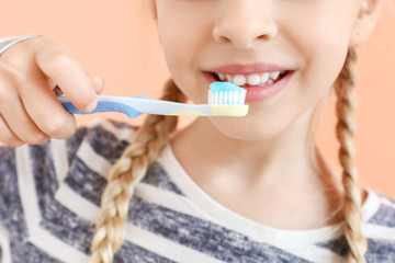 Little girl cleaning teeth on color background, closeup