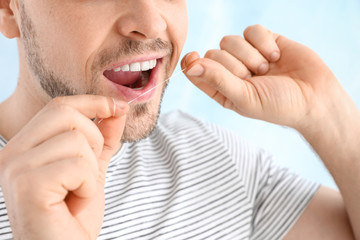 Man flossing teeth on light background, closeup