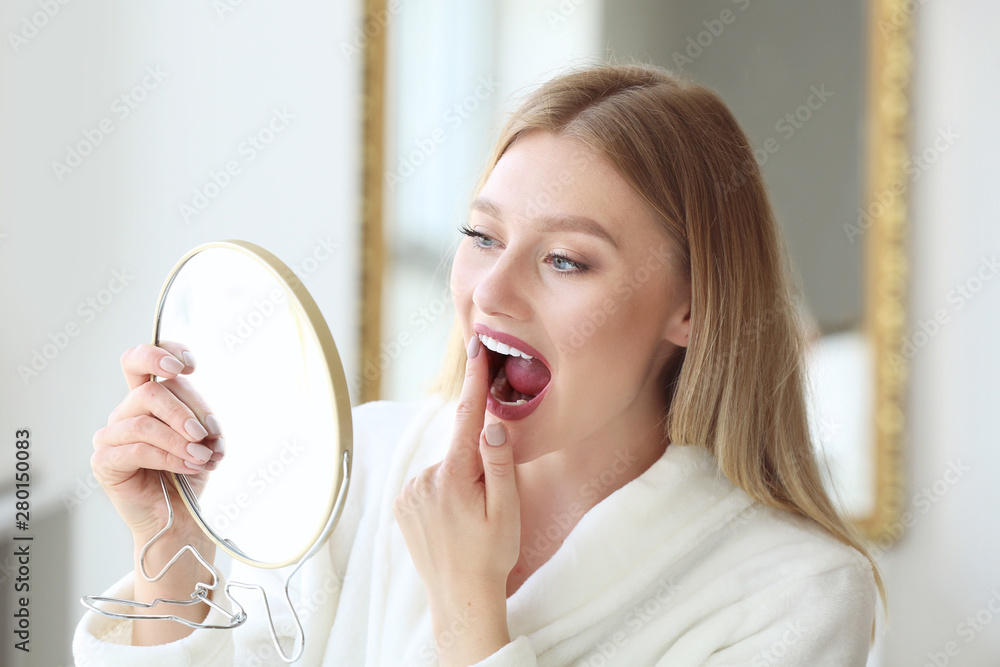 Wall mural Woman checking whiteness of her teeth at home