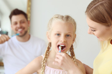 Mother teaching little girl to clean teeth at home