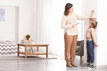 Woman measuring height of her little son near wall