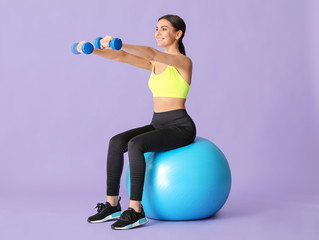 Young sporty woman doing exercises with fitball on color background