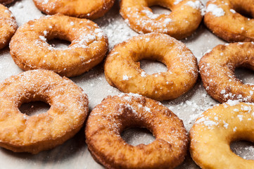 Many homemade baked donuts without cream sprinkled of powdered sugar lies on old rustic wooden table