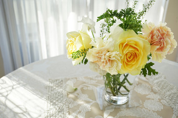 The flower which was displayed to the glass on the table of the room with the window