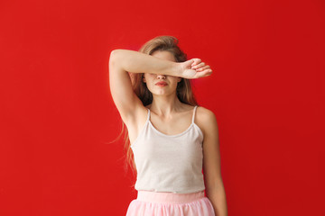 Young woman covering her eyes on color background