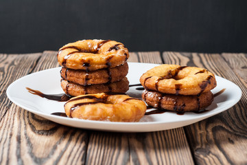 Many homemade baked donuts decorated of chocolate cream lies on white ceramic plate and old rustic wooden table