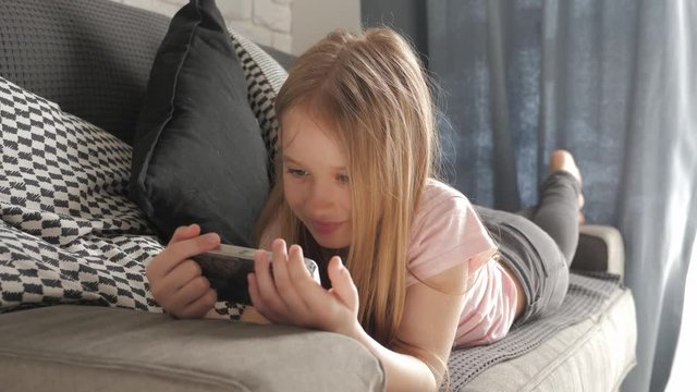Little girl is lying on the bed and looking into her smartphone.