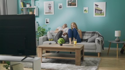 Happy young couple watching tv on couch in cozy living room - Powered by Adobe