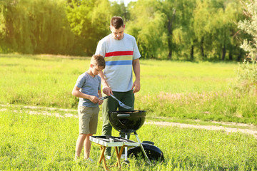 Father with son cooking tasty food on grill outdoors