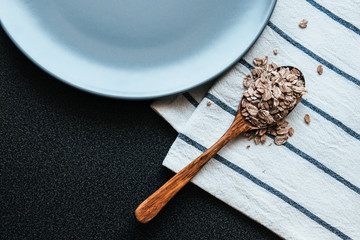 Oats in a wooden spoon grey plate and kitchen towel. Ingredients for healthy breakfast.