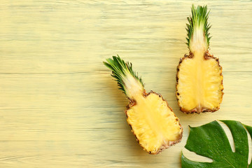 Halves of pineapple and tropical leaf on wooden background